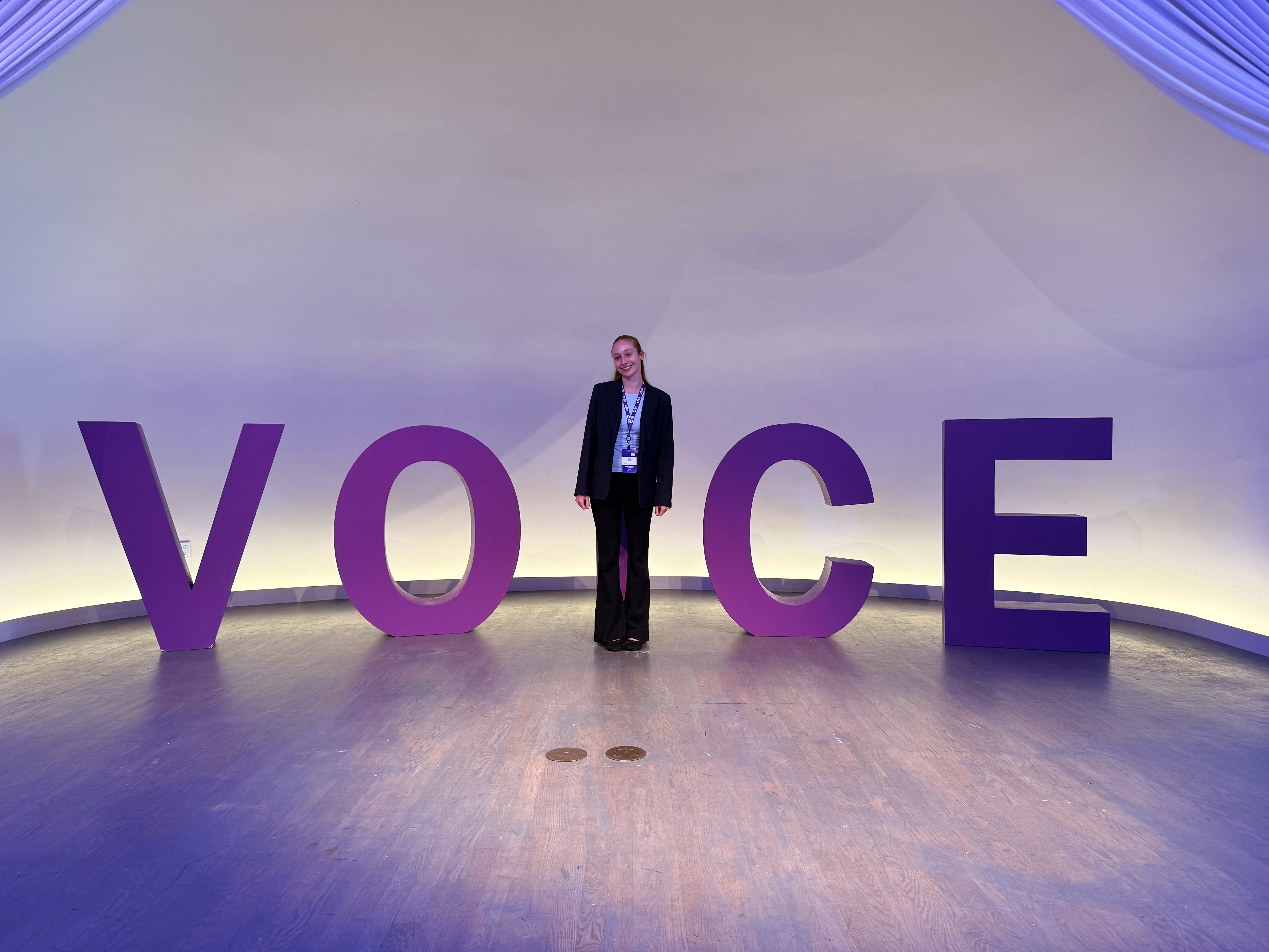 Alisa standing beside oversized VOICE letters at the Voice AI Symposium